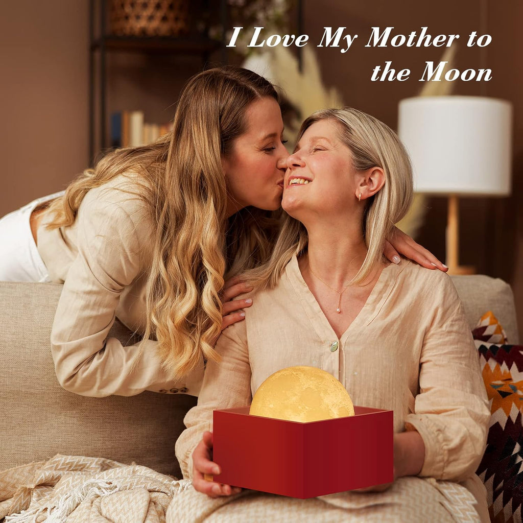 Daughter kissing her smiling mother, who holds a moon lamp in a red gift box